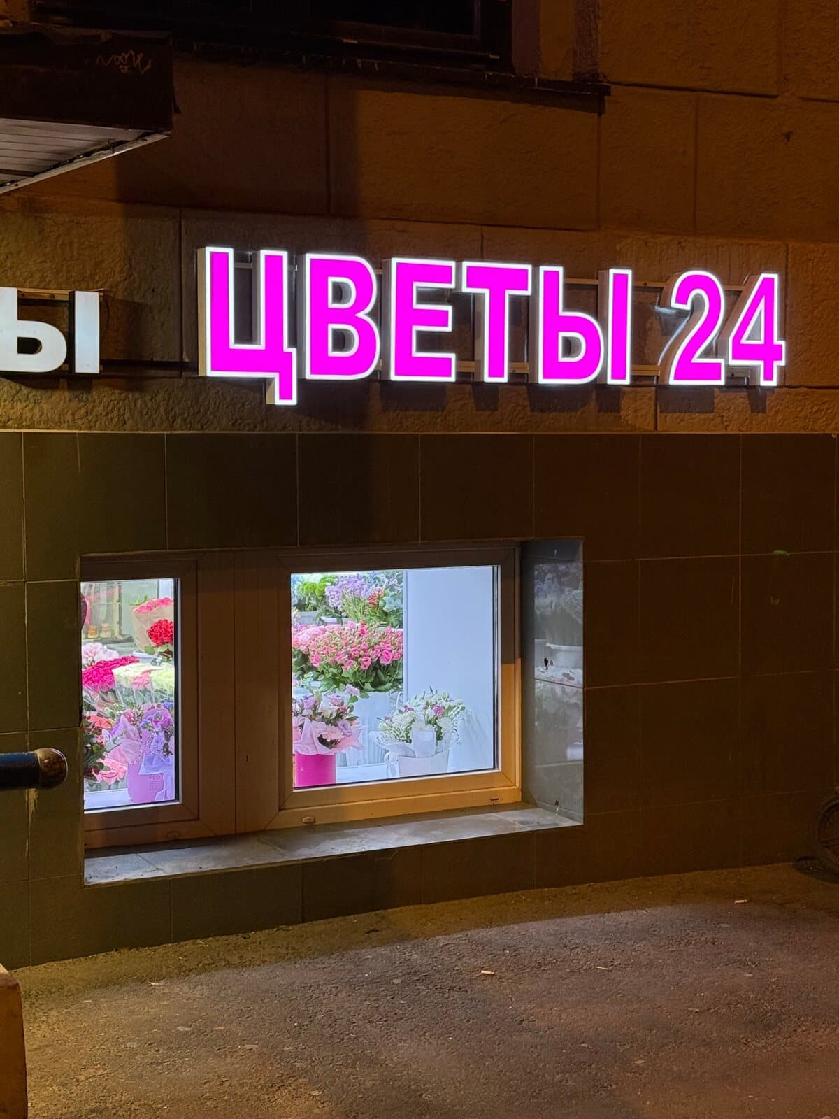 Витрина магазина «Цветы 24» с неоновой вывеской на фасаде дома